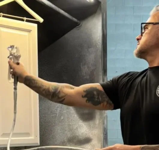 Professional cabinet painter spraying a smooth white finish on a kitchen cabinet door in Salt Lake City