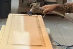 Apply paint to cabinets Applying spray paint evenly on cabinet door for a smooth and durable finish